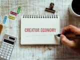 Notebook with the words Creator Economy on a wooden desk with pen and coffee, symbolizing authenticity and digital work