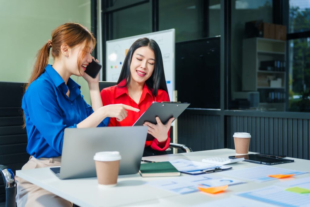 Two women working together on a marketing strategy in a modern office discussing documents and laptop