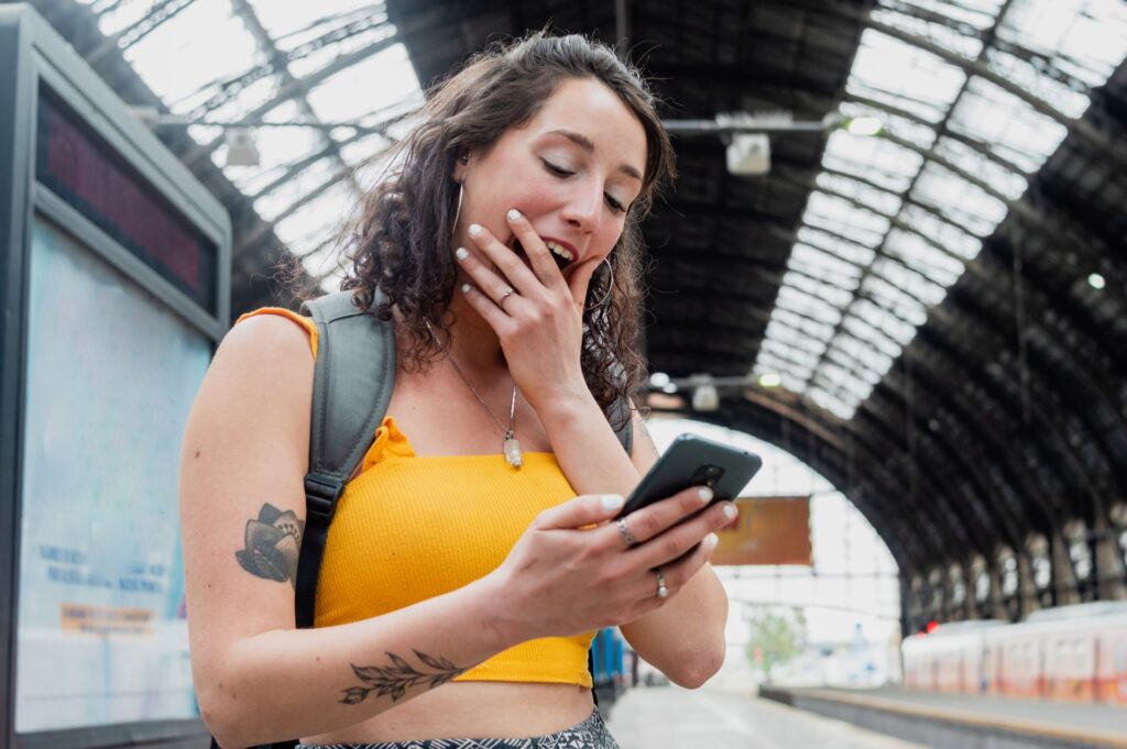 Young woman looks surprised at smartphone while standing in a train station